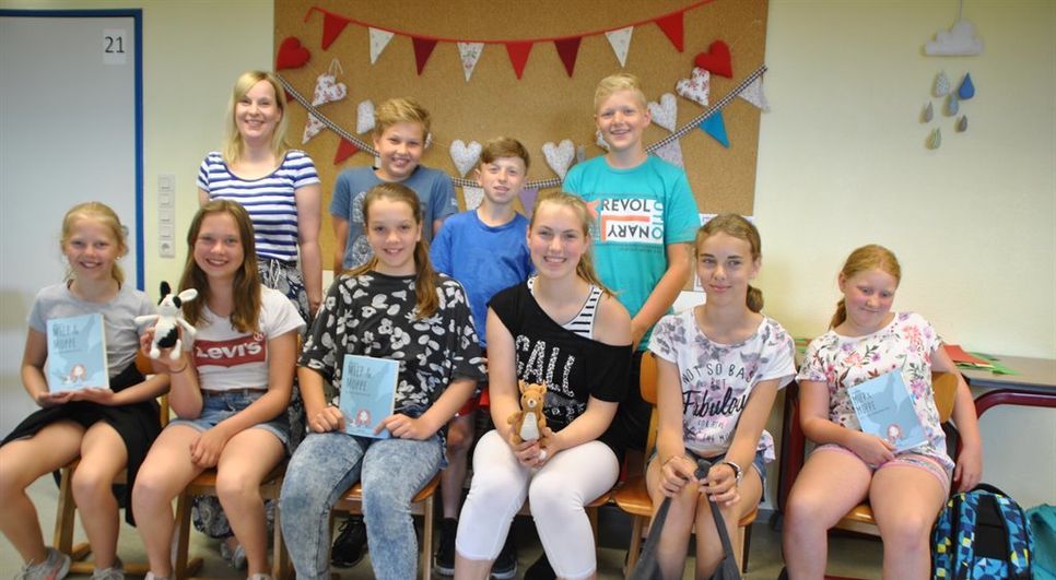 Stolz präsentieren sich ein paar Schüler in Oerel mit der Autorin Stine Oliver (hinten links) und dem Buch „Miep &amp; Moppe“ bei der Lesung. Foto: uml