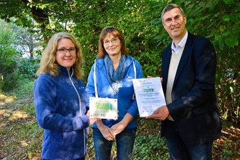 Dr. Maren Meyer-Grünefeldt (v. li.) und Bettina Schroeder freuen sich über das von Karsten Behr überreichte „NATURbegeistert“-Schild.