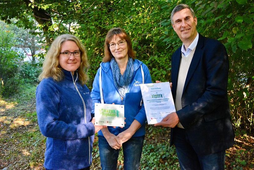 Dr. Maren Meyer-Grünefeldt (v. li.) und Bettina Schroeder freuen sich über das von Karsten Behr überreichte „NATURbegeistert“-Schild.
