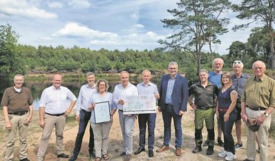 Karsten Behr von der Niedersächsischen BINGO-Umweltstiftung (3. v. li.) überreichte Behlke Mohrmann, 1. Vorsitzende der Jägerschaft Zeven e. V, (4. v. li.) im Beisein weiterer Vertreter:innen der Jägerschaft, der Politik und am Projekt Beteiligter 500 Euro Preisgeld für das „Projekt des Monats Juli“.