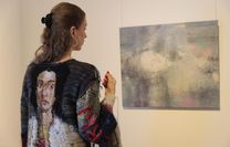 Die Künstlerin Sybille Springer trägt ihr Kunstwerk ›Eine Möglichkeit, den Faden zu spinnen‹, während sie ihr Bild ‹Taylor Swift (Ophelia)‹ betrachtet.