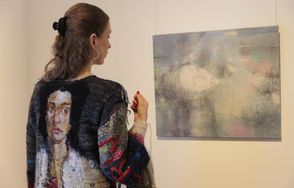 Die Künstlerin Sybille Springer trägt ihr Kunstwerk ›Eine Möglichkeit, den Faden zu spinnen‹, während sie ihr Bild ‹Taylor Swift (Ophelia)‹ betrachtet.