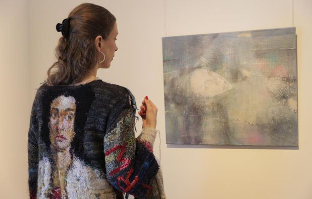 Die Künstlerin Sybille Springer trägt ihr Kunstwerk ›Eine Möglichkeit, den Faden zu spinnen‹, während sie ihr Bild ‹Taylor Swift (Ophelia)‹ betrachtet.