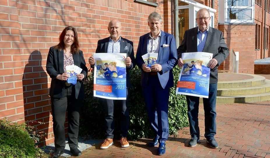 Mareike Wilshusen (v. li.), Bürgermeister Michael Hannebacher, Marco Tulodetzki und Manfred Mühler präsentieren die Plakate und Flyer, mit denen ab sofort Kandidatinnen für den Wirtschaftspreis vorgeschlagen werden können.