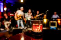 Foto der Music Hall Session, vorne eine beleuchtetes Glas, hinten leicht verschwommen Musiker