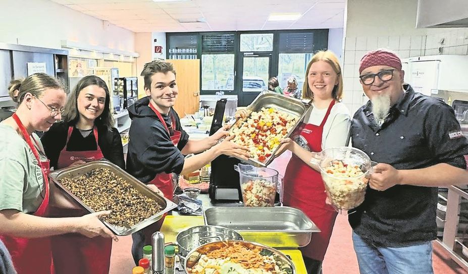 Stolz präsentieren die Schüler:innen ihre Speisen, die sie mit Stefan Marquard (rechts) zubereitet haben.