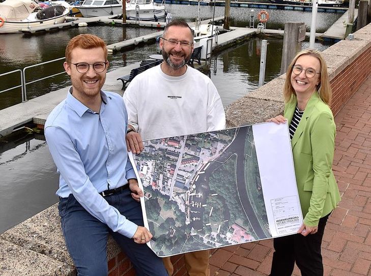 (v. l.) Ortsbürgermeister Dirk-Frederik Stelling, Mario Weichel und Kristin Harms präsentieren den Plan, der den Hafen aufwerten könnte.