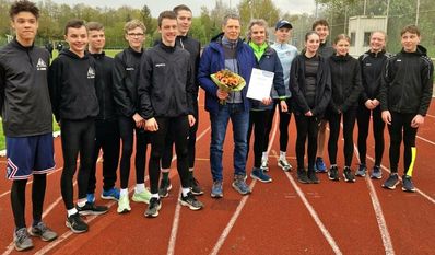 Jan Petermann mit Blumen und Urkunde im Kreise seiner Leichtathleten.