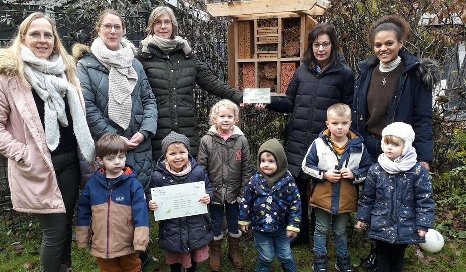 Die Kinder und Fachkräfte vom „Abenteuerland“ versammeln sich vor der neuen Wildbienen-Nisthilfe und freuen sich über den Leitfaden und das Schild für die Kita.