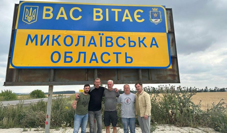 v.li.: Yevhen Tsushko, Peter Göbel, Gerd Brauns, Thomas Wüppermann und Vitalii Porkhun vor einem Schild mit der Aufschrift, die auf deutsch lautet: „Willkommen in der Oblast Mykolajiw“.