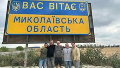 v.li.: Yevhen Tsushko, Peter Göbel, Gerd Brauns, Thomas Wüppermann und Vitalii Porkhun vor einem Schild mit der Aufschrift, die auf deutsch lautet: „Willkommen in der Oblast Mykolajiw“.