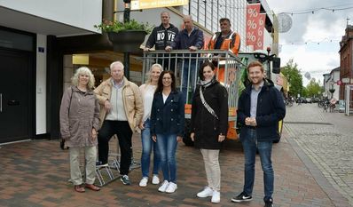 Mitarbeiter vom städtischen Bauhof (im Baggerkorb), Mitglieder des Ortsrates und BSCM-Managerin Bärbel Hensel (2 v.r.) sowie Ortsbürgermeister Dirk-Frederik Stelling (re.) freuen sich über die neu angebrachte Blumenpracht.