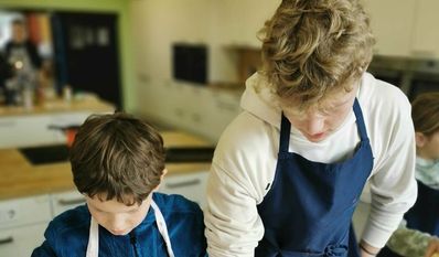 Thore Mangels, Mitarbeiter der Abteilung BISTRO zeigt Viertklässler, wie man Zwiebeln schneidet.